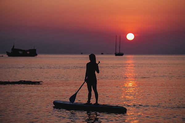 Silhouette image of a young woman on stand up paddle board in a sea before sunset.